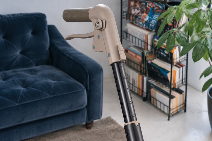 A single rollator handle and brake lever above a telescoping height-adjustment stem in a living room.