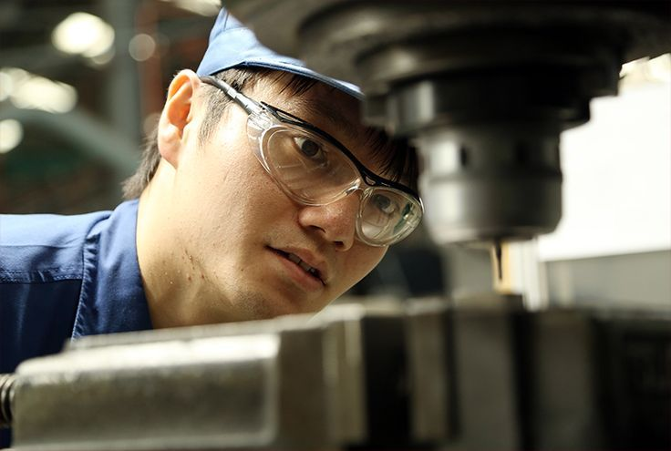 A worker wearing safety glasses concentrating beside industrial machinery